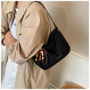 Detail of black matte shoulder bag with vintage wooden beads tassel on a model