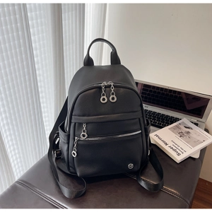 Macro shot of black pebbled leather backpack showing silver zippers and metal logo detail