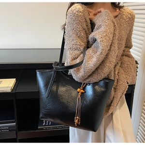 Close-up of black leather tote bag with wooden gourd pendant and tassel detail