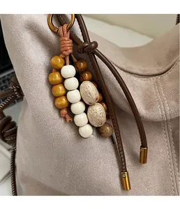 Detail eines Taschenanhängers aus Holzperlen mit geflochtenem Seil an Wildledertasche