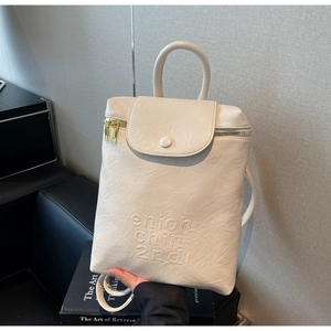 Détail du sac à dos beige souple avec lettres embossées et fermeture éclair dorée