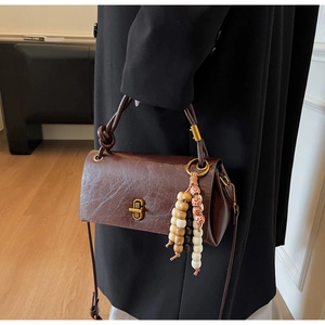Detail view of deep brown vintage leather handbag with gold twist lock and wooden beads
