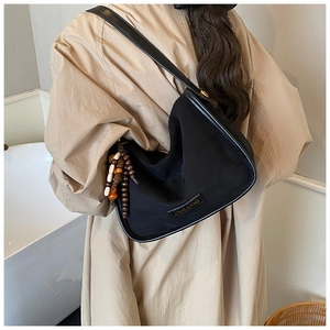 Close-up of black crossbody bag with wood bead tassel and metal brand logo detail