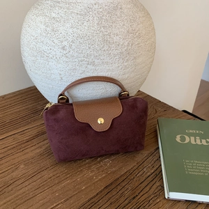 Close-up of burgundy suede handbag with brown leather trim on vintage wooden table