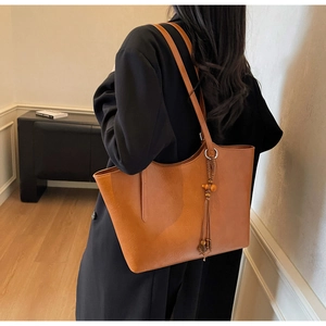 Detailed side view of caramel leather tote bag with wooden bead and tassel keychain charm