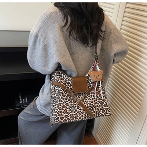 Detail view of leopard print tote bag with brown flap and teddy bear charm on shoulder