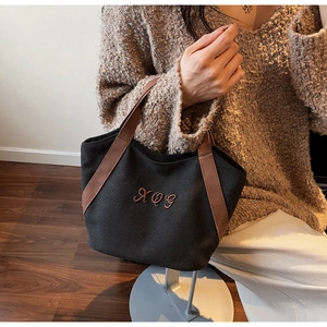 Close-up of black canvas tote bag featuring brown XQG embroidery and wide woven handles