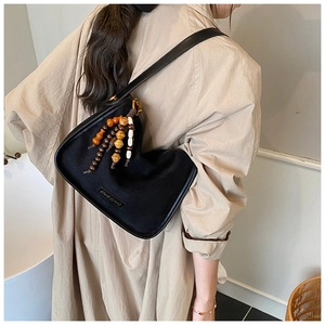 Detail of a black crossbody bag with multi-color wooden bead tassel and leather strap