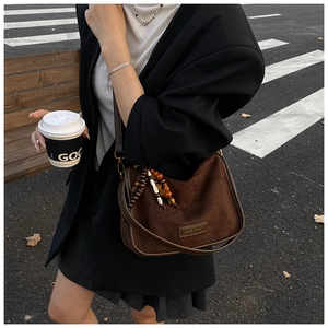 Detail of brown frosted leather hobo bag with ethnic beaded tassel and metal logo plate