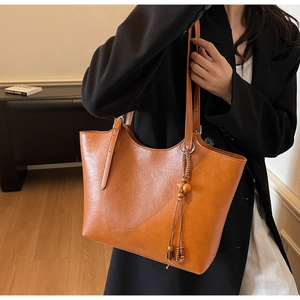 Detail of vintage caramel tote bag with wooden bead tassel on a model in home setting