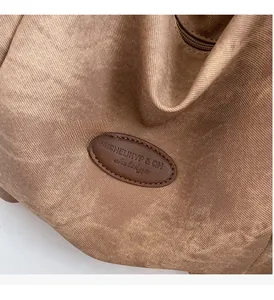 Close-up of khaki woven fabric detail with brown leather logo patch and fine stitching