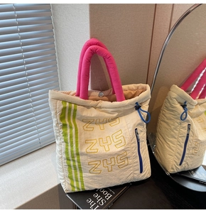 Detail of quilted beige tote bag with pink handles and blue functional zippers