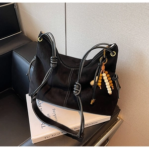 Detail der schwarzen Wildleder-Hobo-Tasche mit Kontrastnähten und Perlenanhänger