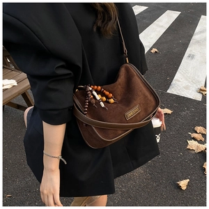 Close-up of brown matte crossbody bag featuring metallic logo and ethnic tassel detail