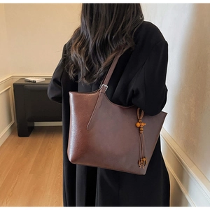Detail of vintage brown tote bag featuring wooden bead tassels and adjustable strap