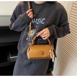 Detail of vintage caramel leather crossbody bag with wooden bead tassel and metal rotary lock