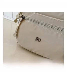 Nahaufnahme der beigen Nylon-Umhängetasche mit Reißverschlüssen und Metall-Logo-Detail