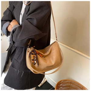 Detail of khaki suede crossbody bag featuring wooden bead tassels and logo leather patch