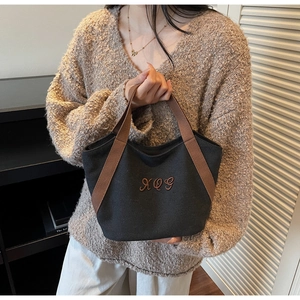 Detail of black canvas tote bag featuring brown XOG embroidery and woven handle straps