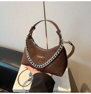 Gros plan d'un sac demi-lune en daim marron avec chaîne argentée et logo texte blanc