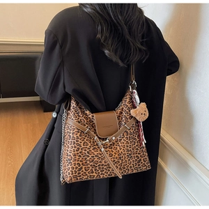 Detail of leopard print tote bag featuring a leather flap closure and a plush bear charm