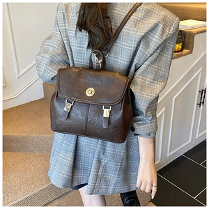 Close-up of retro brown backpack with gold hardware worn over a grey checkered blazer