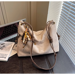 Detail der beigen Wildleder-Hobo-Tasche mit dickem geflochtenem Seilriemen und Perlenanhänger