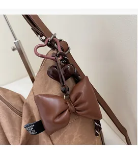 Detail of a brown leather bow and glossy heart charm on a canvas shoulder bag