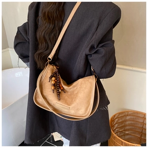 Close-up of brown suede hobo bag with wood bead tassel and logo detail on gray blazer