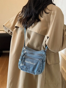 Blue denim crossbody bag with multi-zipper compartments and embroidery on beige coat