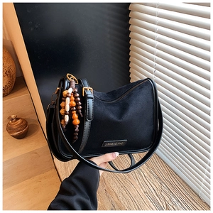 Detail of matte black shoulder bag with beaded ethnic charm and metal logo badge