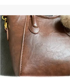Dettaglio della borsa in pelle marrone con trama litchi, fibbia dorata e ciondolo di peluche