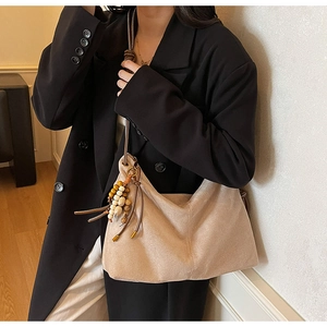 Detail der Wildleder-Hobo-Tasche mit braunem Lederriemen und hölzernem Perlenanhänger