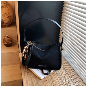 Detail of black suede shoulder bag with wood bead tassel on a wooden desk setting