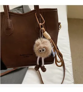 Dettaglio della borsa a secchiello in pelle marrone con ciondolo a forma di bambola