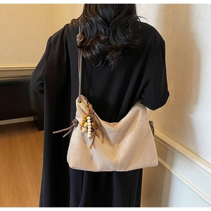 Detail der beigen Wildleder-Hobo-Tasche mit bunten Holzperlen an schwarzem Mantel