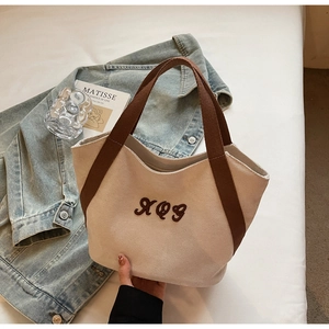 Detailed close-up of a cream canvas tote bag with brown straps and XQG embroidery