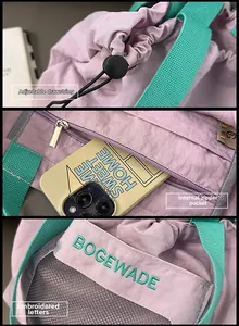 Detail of purple nylon tote with drawstring closure, inner zip pocket and green embroidery