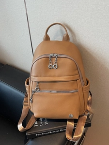 Brown litchi grain leather backpack with silver zippers on a black leather chair