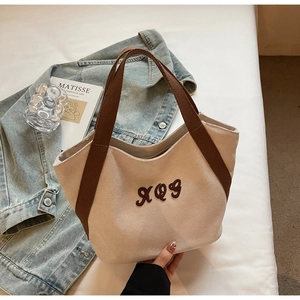 Close-up of beige canvas tote bag with brown embroidered XQG logo and durable webbing handles