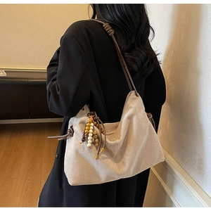 Detail der minimalistischen Wildleder-Beuteltasche mit Flechtriemen und Holzperlen-Quasten