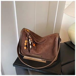 Detail of dark brown suede hobo bag with colorful wooden bead charm and metal logo plate