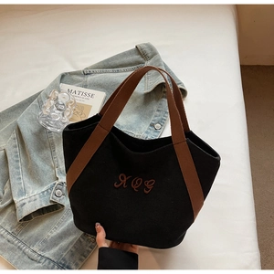 Close-up of black canvas tote bag featuring brown XQG embroidery and reinforced handles