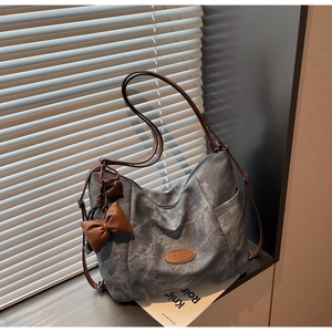 Detail of dark grey tote bag with brown leather straps and heart charm in natural sunlight