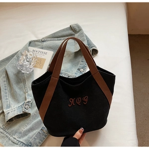 Detail of black canvas tote bag with brown handles and embroidered letters