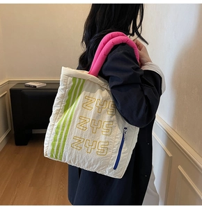 Close-up of white quilted tote bag with pink handles and green stripes worn by a model