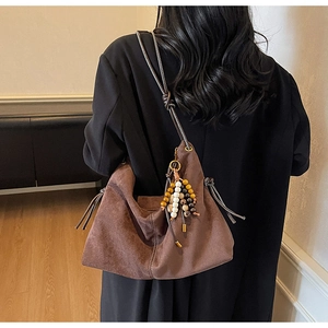 Detail einer braunen Wildleder-Hobo-Tasche mit Perlenquaste und geknotetem Schultergurt