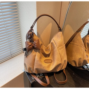 Detail of khaki tote bag featuring brown leather straps and a decorative bow heart charm
