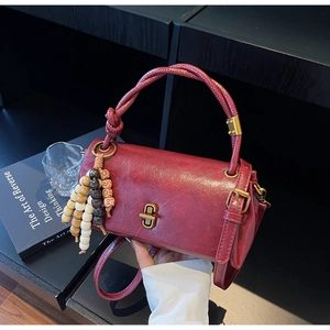 Detail of burgundy oil wax leather cylinder bag with gold twist lock and beaded tassel