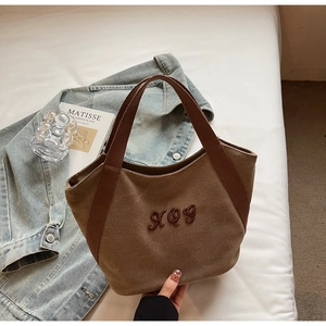 Detail of a brown canvas tote bag featuring premium XQG letter embroidery and sturdy handles